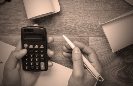Engineer workspace. Male hands count on the calculator the cost of building a house on a wooden...