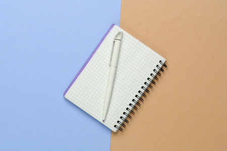 Notebook with pen on a yellow-blue pastel background. Top view