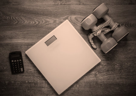 The concept of weight loss, fitness. Calorie Counting. Floor heights, calculator and dumbbells, measuring tape on wooden floor. Top viewの写真素材