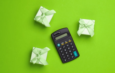 Calculating the value of the gift. Gift boxes and calculator on green background. Top viewの写真素材