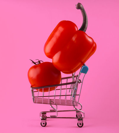 Shopping trolley with bell pepper and tomato on pink background. Supermarket conceptの写真素材
