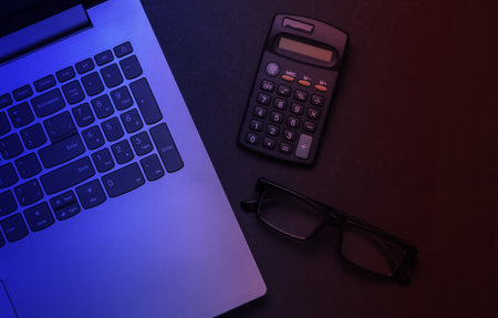 Laptop, glasses, calculator in neon light. Top view.の写真素材