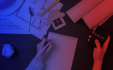 Engineering workspace. Female hands make calculations and write in notebook information in neon...