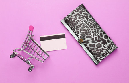 Stylish wallet, shopping trolley and bank card on pink background. Shopping concept. Top view