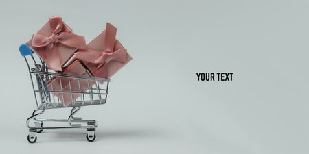 Shopping trolley and gift boxes with bows on white background. Composition for christmas, birthday or wedding. Copy spaceの写真素材