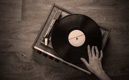 Female hands set up a retro vinyl record player on a wooden floor. Music lover, 70s, nostalgia, top viewの写真素材