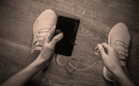 Woman in sportswear sitting on the floor in the room chooses music on smartphone with earphoness for future workout or jogging. Top viewの写真素材