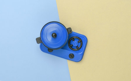 Toy plastic stove with pan on yellow blue pastel background. Kid's Kitchen. Top view, minimalism