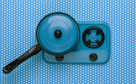 Toy plastic stove with pan on blue polka dot tablecloth. Kid's Kitchen. Top view, minimalismの写真素材