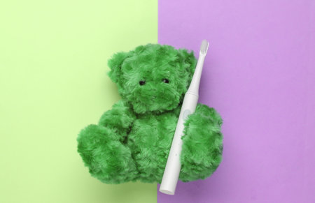 Teddy bear holds a toothbrush on a pink green background. Teeth care. Top viewの写真素材