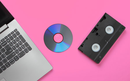 Flat lay composition of laptop, cd disc, audio cassette on pink background. Retro storage media. Top...