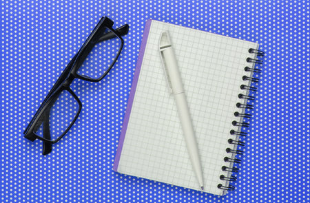 Notebook with pen and glasses on a polka dot tablecloth. Top viewの写真素材