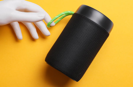Plastic hand holding bluetooth speaker on yellow backgroundの写真素材
