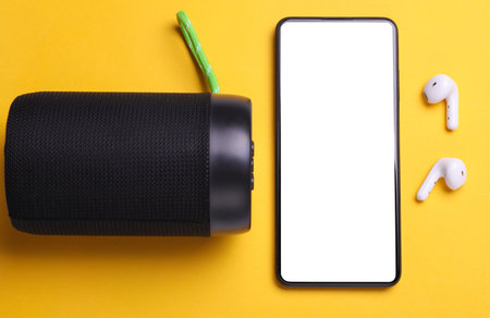 Wireless bluetooth stereo speaker with smartphone and earphones on yellow background. Top viewの写真素材