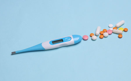Modern electronic thermometer with tablets on a blue background. Diagnosis and treatment of colds and fluの写真素材