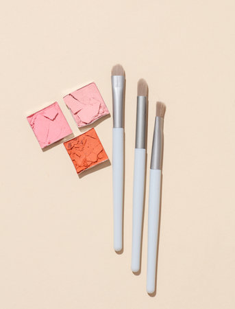 Crushed eyeshadow for makeup with brushes. Cosmetic product sample on beige background. Creative...