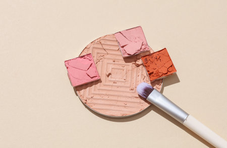 Crushed eyeshadow for makeup with brush. Cosmetic product sample on beige background. Creative...