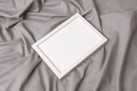 White blank photo frame lies on the bed sheet