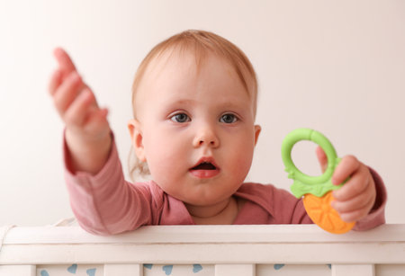 Little baby playing with a toy in a crib with a side