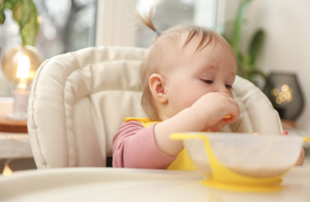 Cute little baby girl eats on her own at the feeding tableの写真素材