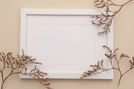 Mockup of white photo frame with dry grass on beige background. Top view