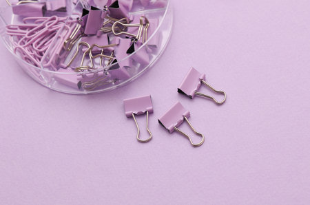 Set of purple paper clips, binders and pins with box on lavender background