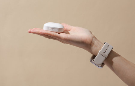 Female hand holding case with wireless earbuds on beige backgroundの写真素材