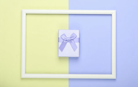 Gift box on blue yellow pastel background with white frame. Studio shot. Creative flat lay. Top...