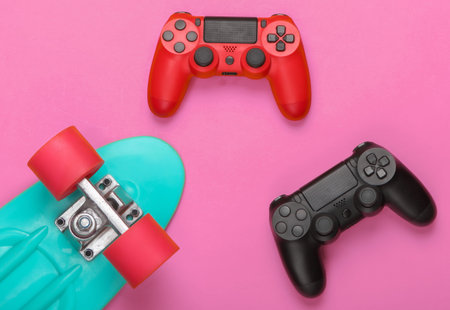 Gamepads with cruiser board on pink background. Childhood concept, summer fun, entertainment. Top...