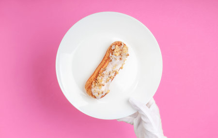 Waiter in white gloves serves eclair on a plate. Pink background. Dessert. Restaurant food. Top...