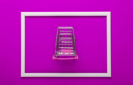 Mini shopping trolley on pink background with white frame. Studio shot. Creative flat lay. Top view....