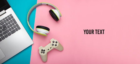 Laptop with headphones, gamepad on pink blue background. Copy space. Gaming, entertainment or...