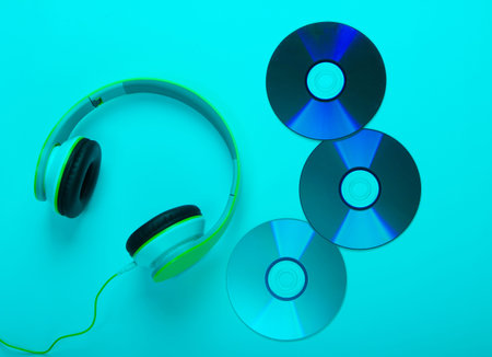 Stylish wired stereo headphones and cd discs with blue neon light. Music lover. Retro 90s. Top view.