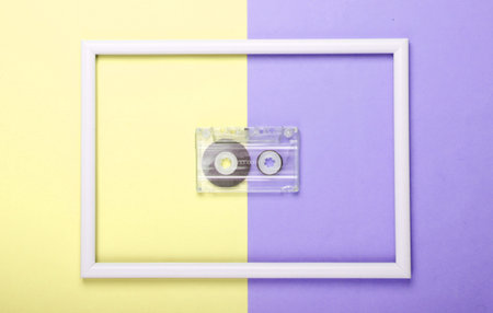 Audio cassette on yellow purple pastel background with white frame. Studio shot. Creative retro flat...