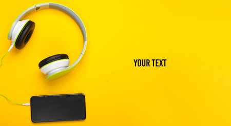 Stylish wired stereo headphones with smartphone on yellow background. Copy space. Music lover. Modern gadgets. Top view. Minimalism