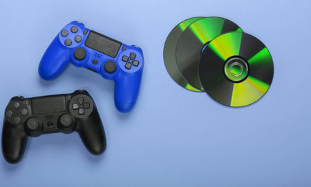 Two gamepads and cd compact discs on blue pastel background. Gaming, entertainment concept. Top view