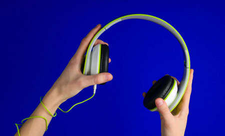 Hands wrapped in cable holding stereo headphones on blue background