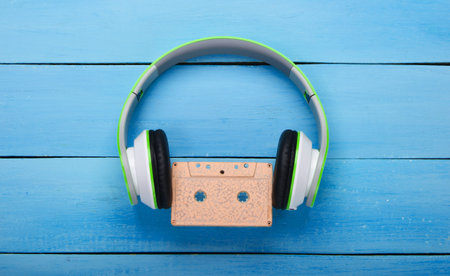 Stereo headphones with audio cassette on blue wooden table. Music lover. Retro 80s. Top view.