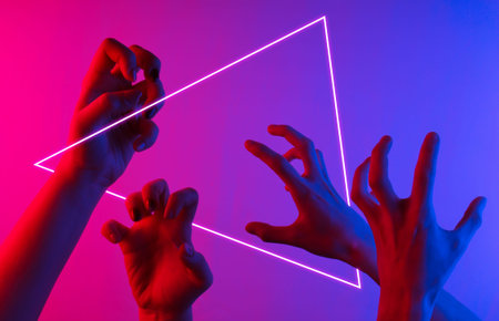 Halloween concept. Female hands with scary gestures. Neon blue-pink gradient light. Night glow. Triangle.の写真素材