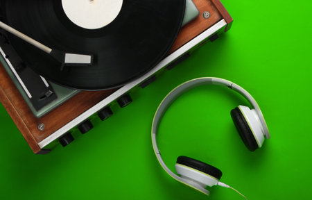 Retro vinyl record player with stereo headphones on green background. Top view