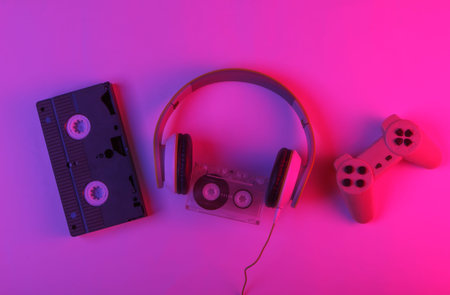 Retro media and 80s entertainment. Headphones, audio cassette, video cassette, gamepad. Neon...