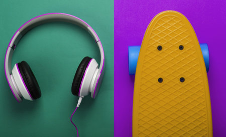 Cruiser board and stereo headphones on a green-purple background. Summer fun. Top view