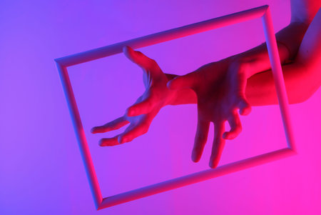 Creative art. Female hands through a soaring frame with neon holographic light. Gradient glow. Pop...