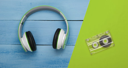 Stereo headphones with audio cassette on blue wooden table. Music lover. Top view.