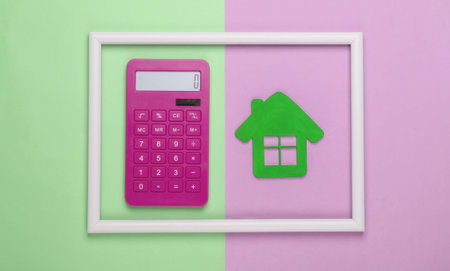 Calculator and green house in a white frame on pink green background. Concept art photo. Top view. Minimalismの写真素材