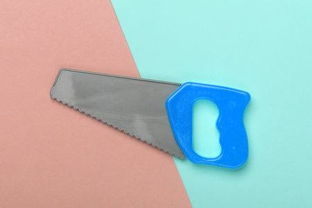 Toy mini plastic saw on a blue-pink pastel background. Top viewの写真素材