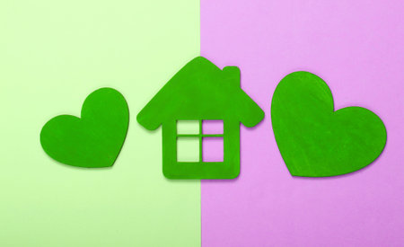 Green wooden hearts with a house figurine on pink green pastel backgroundの写真素材
