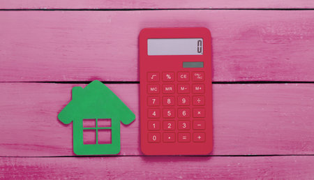 Calculator with a house figure on pink wooden background. Calculation of rent value