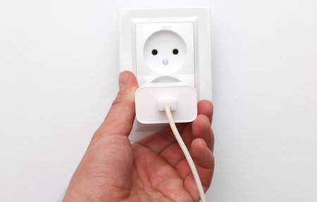 Hand inserting charging block into electrical outlet on white background