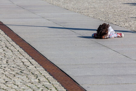 small child sitting bored on the road asphaltの写真素材